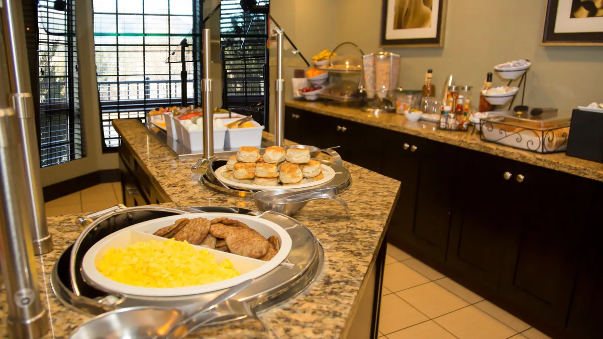 A well-appointed breakfast buffet is set up on a granite countertop in a cheerful dining area. There's a tempting spread of breakfast items ready for guests, with ample space to gather and socialize before starting the day.