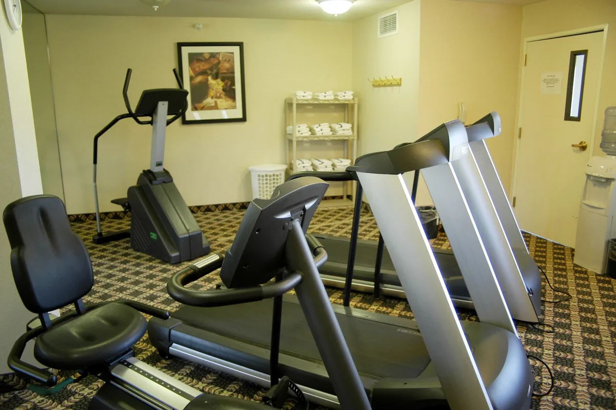 This image shows a well-equipped fitness center featuring multiple treadmills and an elliptical machine, positioned in a spacious, brightly-lit room. A water cooler provides refreshment, and motivational touches suggest an energizing environment.