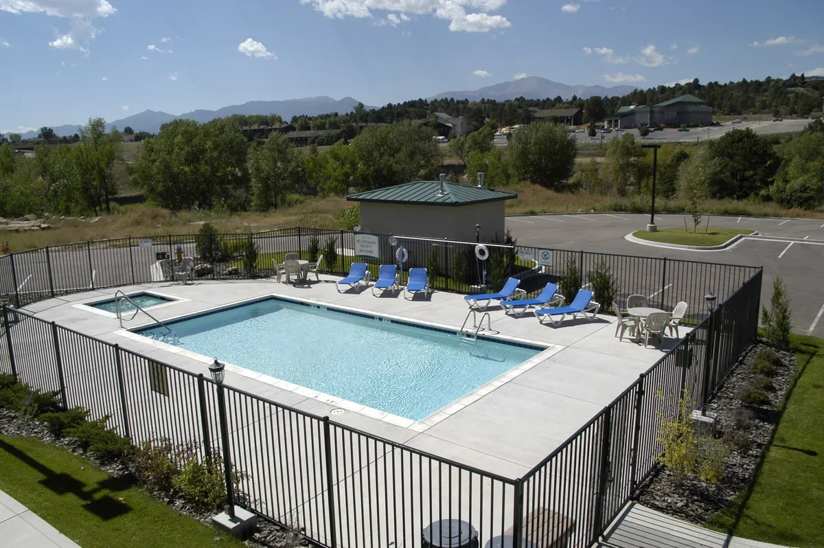 This exterior image captures a vibrant swimming pool area surrounded by comfortable lounge chairs and lush landscaping. The scene is lively, featuring children playing in the water and families relaxing poolside. The pool house and sun-soaked setting evoke a welcoming, resort-like atmosphere.