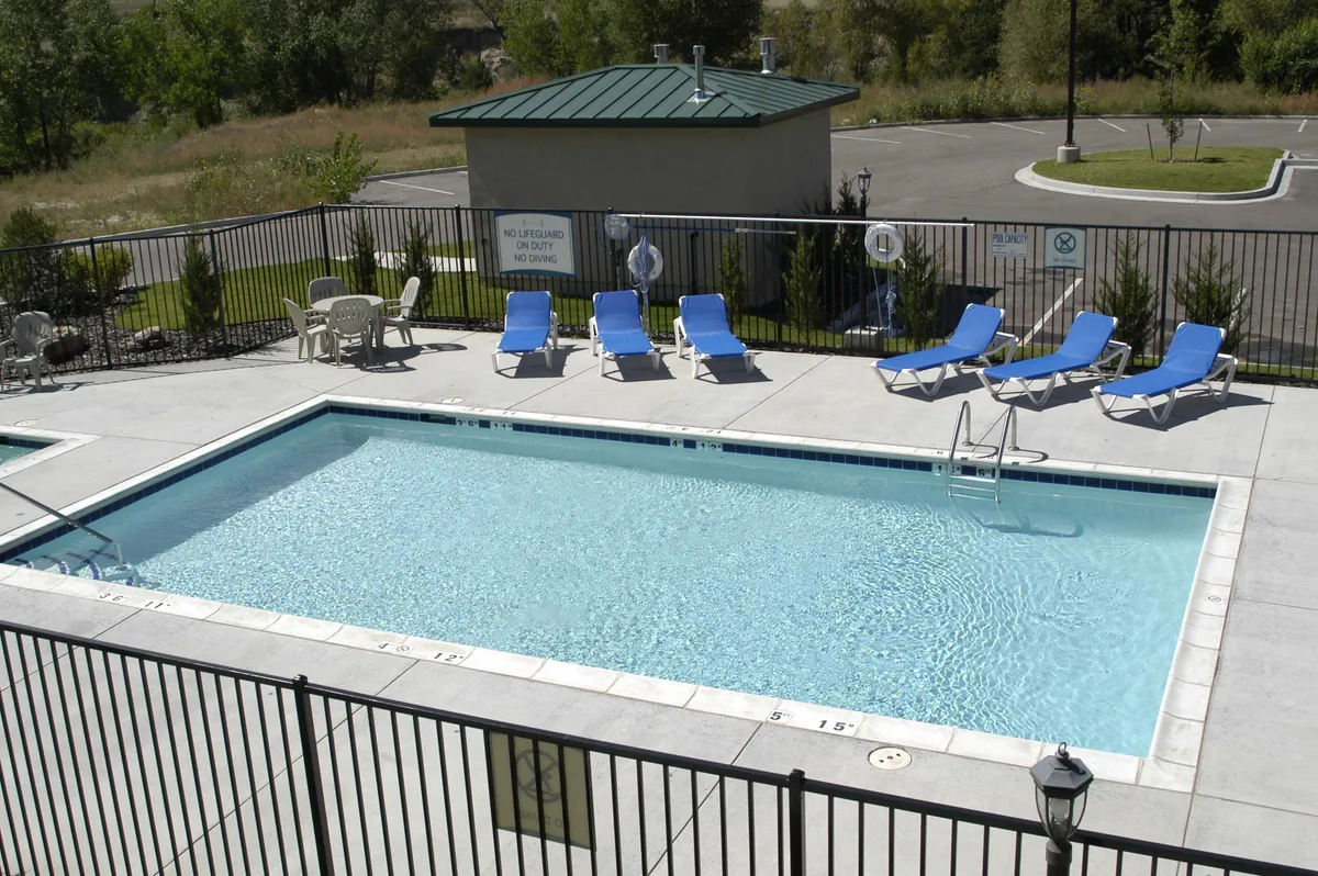 This image features the outdoor swimming pool framed by lounge chairs and a poolside fence, with a lifeguard station visible in the scene. The tranquil mood is enhanced by soft lighting, suggesting a relaxed afternoon or early evening environment where guests can unwind, sunbathe, or enjoy a swim.