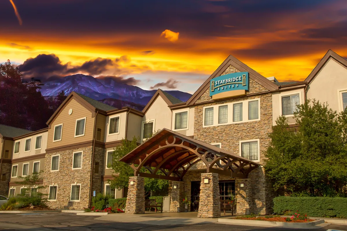 The hotel entrance features a welcoming awning, stylish stone facade, and clear signage. Well-maintained outdoor seating and garden areas create an inviting first impression and hint at communal spaces for guests to enjoy.