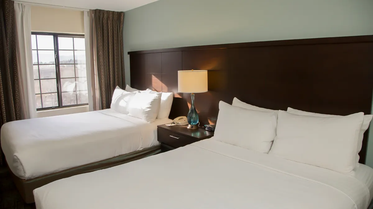 A spacious bedroom containing two cozy Queen beds, each with its own lamp and nightstand. A window lets in sunlight, and the arrangement encourages both privacy and togetherness for family or friends sharing the space.